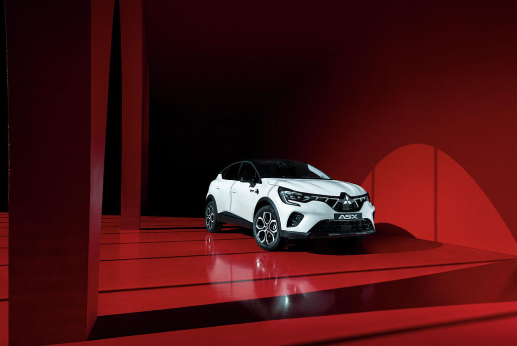 Nowe Mitsubishi ASX w kolorze białym, zaparkowane na czerwonym parkingu.