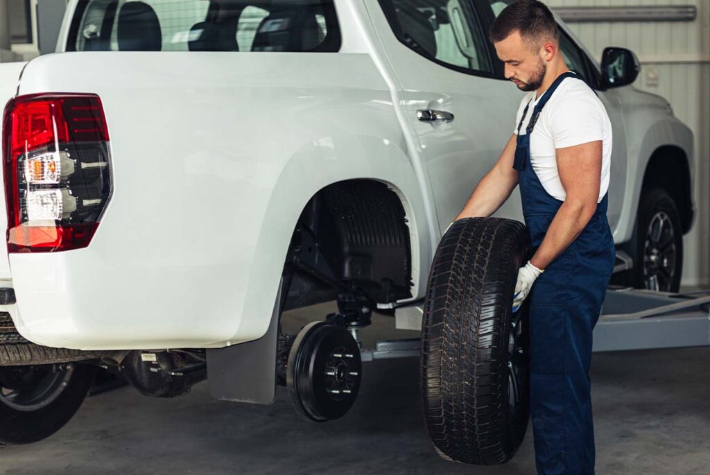 Wymiana koła przez mechanika w białym pickupie Mitsubishi L200.