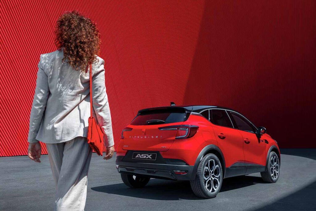 Modelka w białym garniturze idzie w kierunku czerwonego Mitsubishi ASX.
